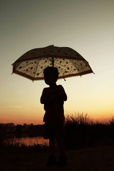 Happy child with an umbrella silhouette on nature in the park su — Stock Photo, Image