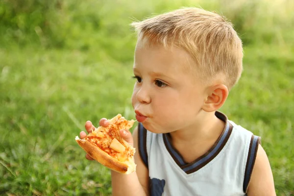 Criança comendo uma pizza saborosa sobre a natureza da grama no par — Fotografia de Stock