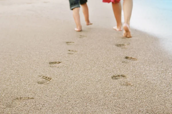 Happy parents with baby are traces on the sea sand outdoors — Stock Photo, Image