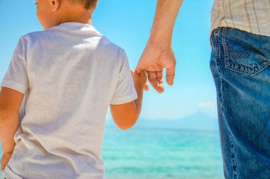 Mutlu baba, Yunan Denizi kıyısında bir çocuğun elini tutuyor.