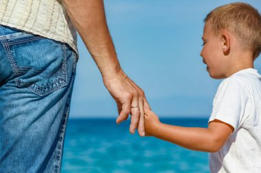 Mutlu baba, Yunan Denizi kıyısında bir çocuğun elini tutuyor.