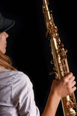 Siyah arka plandaki bir kızın elinde soprano saksafon.