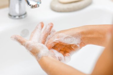 Musluğun altında sabun ve su ile yıkanan eller.