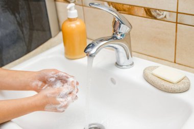 Musluğun altında sabun ve su ile yıkanan eller.