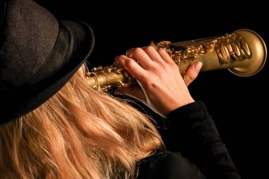 Siyah arka plandaki bir kızın elinde soprano saksafon.