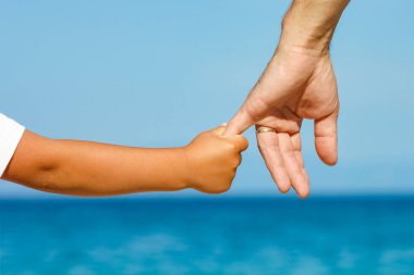 Mutlu baba, Yunan Denizi kıyısında bir çocuğun elini tutuyor.