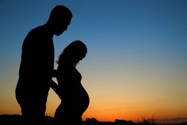 Gün batımında aşık hamile bir çiftin silueti.