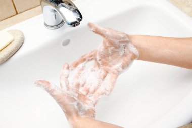 Musluğun altında sabunla ellerini yıkamak, suyla.