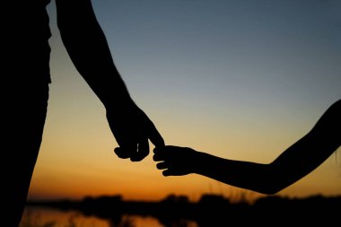 Siluet ebeveyn küçük bir çocuğun elini tutar.