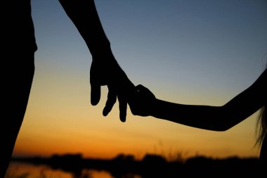 Siluet ebeveyn küçük bir çocuğun elini tutar.