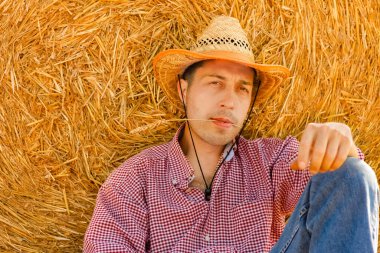 Samanlığın yanındaki samanlıkta bir kovboy. Balyalar sahada mutlu bir adamla.