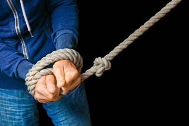 Siyah arka planda tehdit oluşturan bir iple bağlanmış eller. İş hayatında kölelik, insanlara karşı şiddet demektir..