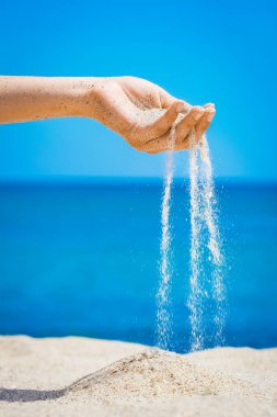 Bir el, doğaya yolculukta denizden kum döker. Deniz kumlarında tatiller geçer..