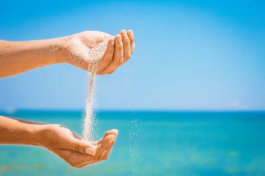 Bir el, doğaya yolculukta denizden kum döker. Deniz kumlarında tatiller geçer..