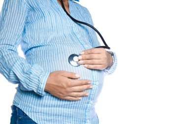 Elinde statoskop olan hamile bir kadın beyaz bir arka planda yatıyor. Yakında doğacak olan karnındaki bebeği dinler..