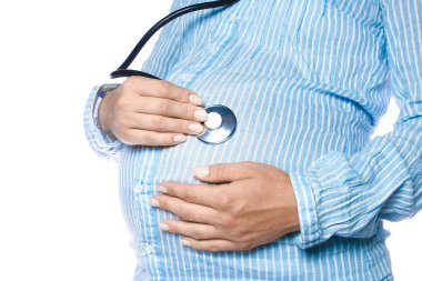 Elinde statoskop olan hamile bir kadın beyaz bir arka planda yatıyor. Yakında doğacak olan karnındaki bebeği dinler..