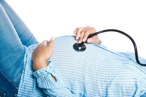 一个手里拿着听诊器的孕妇躺在白色的背景上 倾听肚子里即将出生的婴儿的声音 — 图库照片