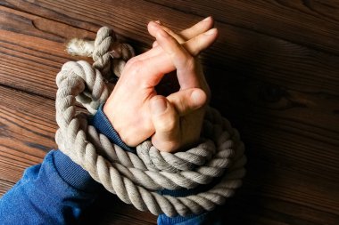 Ahşap bir arka planda hayatı tehdit eden bir iple bağlanmış eller. İş hayatında kölelik insan istismarıdır..