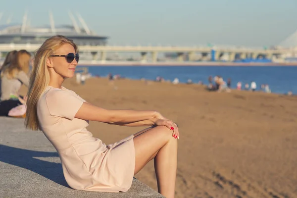 Belle femme blonde en lunettes de soleil assise sur une plage de sable — Photo