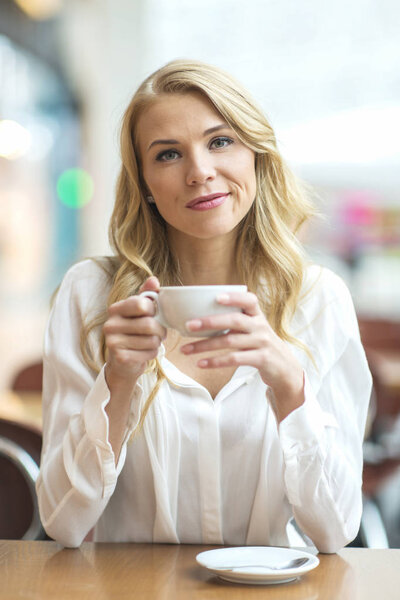 Young blonde sitting in a cafe, drinking coffee and looking into