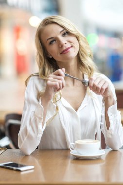 Çekici genç sarışın bir kafede oturan ve kahve içme