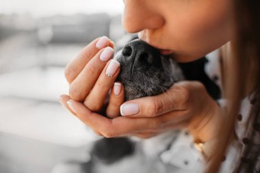 Genç bir kadın köpek burnunu öpüyor.