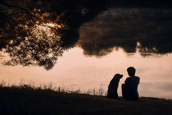 Woman and dog silhouettes view, sitting by the river together in summer — 스톡 사진