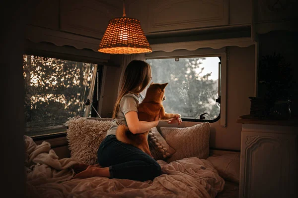 Young woman and dog looking out the window from inside the trailer home — Stock Photo, Image
