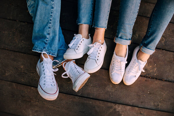 three people legs in white trainer shoes on wooden floor