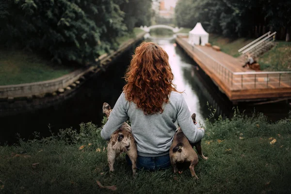 Woman with red curly hair sitting outdoors with two dogs, rear view — Stock Photo, Image