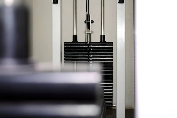 Black weight stack on metal tubes. Part of cable crossover training machine in the gym. Blurred stack on the foreground.