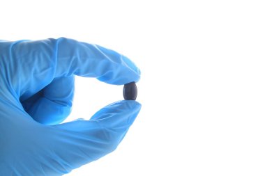 Elinde koyu bir Astaxanthin hapı var. Mavi tıbbi nitril eldiven giyiyor..