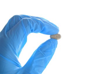 Elin yatay olarak multivitamin kompleksi hapı tutuyor. Mavi tıbbi nitril eldiven giyiyor..