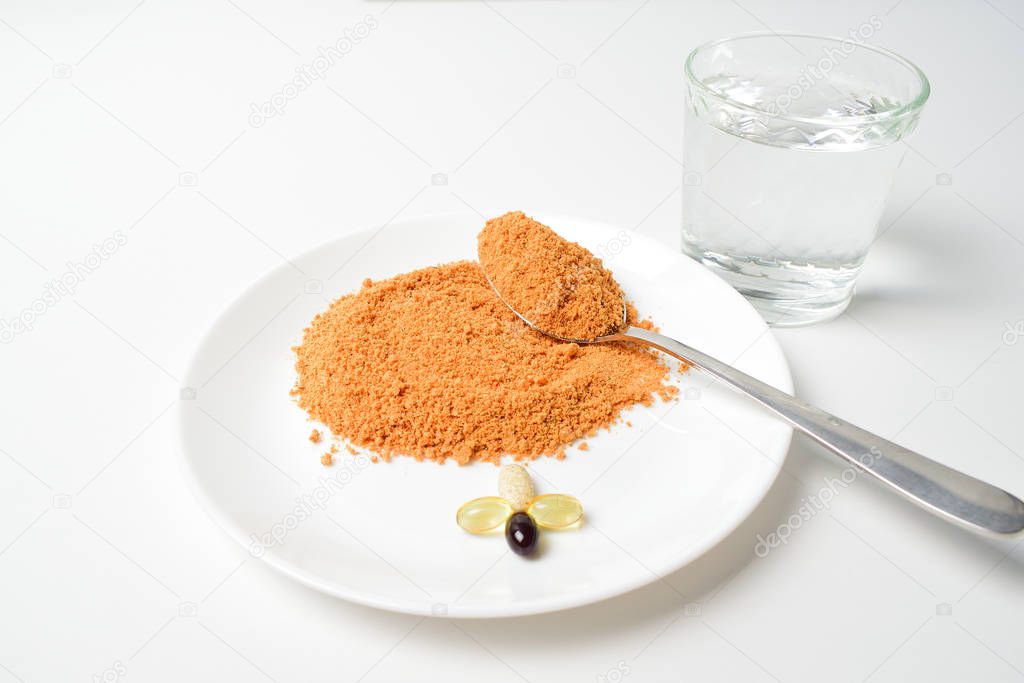 Tomato protein soup powder on a spoon. Hand puts the powder into the glass of water. Meal replacement. Dry soup. Multivitamins, astaxanthin, fish oil, omega pills.  Closeup.