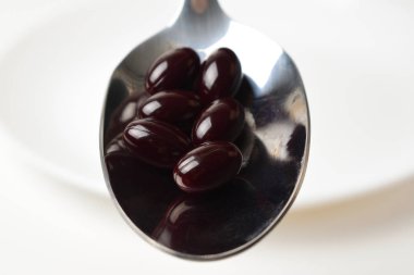 Astaxanthine pills in the spoon on a white plate background. Close-up