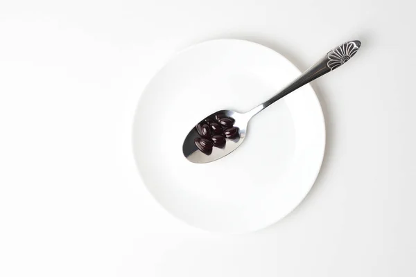 Astaxanthin capsules in the spoon on a white plate background. Top view.