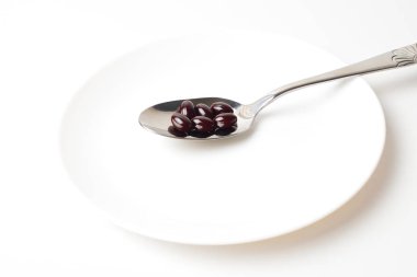 Astaxanthin capsules in the spoon on a white plate background. 