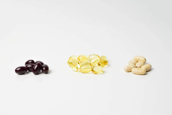 Huile de poisson, multivitamines et capsules d'astaxanthine en trois grappes. Oméga-3 au milieu. Fond blanc. Gros plan . — Photo