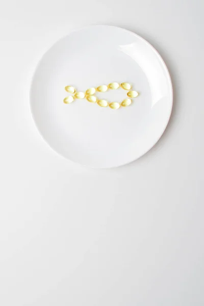 Bir tabakta Omega-3 doymamış yağ asitleri. Balık yağı, beyaz tabakta balık şeklinde softgeller. Yemek değişimi. Günlük beslenme reçetesi. Boşluğu aşağıya kopyala.