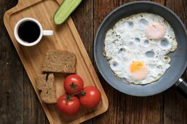 Kahvaltıda. Tahta bir masanın üzerinde sade kahve, yumurta, domates, salatalık ve ekmek kahvaltısı..