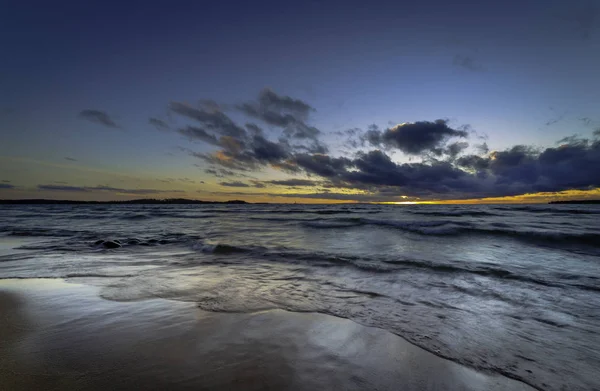 Κύματα βιασύνη επάνω σε μια αμμώδη παραλία στο ηλιοβασίλεμα — Φωτογραφία Αρχείου