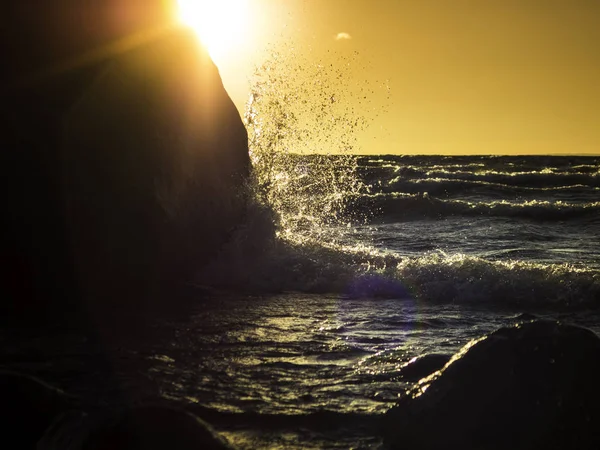 Ola que salpica sobre una gran roca y con el sol en la espalda —  Fotos de Stock