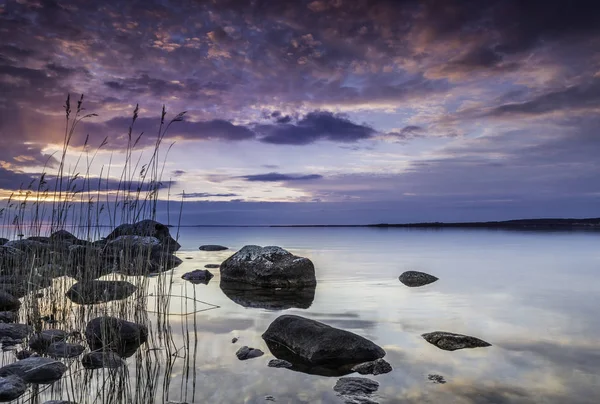Färgsprakande solnedgång vid en sjö med stenig strand — Stockfoto