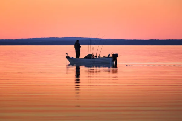 Un homme pêche depuis un petit bateau au coucher du soleil — Photo