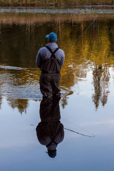 Mann mit Watstiefeln mit blauer Mütze steht im Fluss Fliegenfischen. — Stockfoto