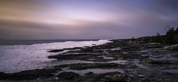 Lång exponering bild av klippor och snö vid havet — Stockfoto