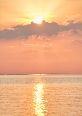 Yelkenli bir gölde yelken açıyor, güneş bulutların ardında.
