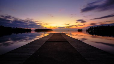 Arka planda günbatımı olan bir göle giden büyük bir iskele.