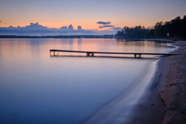 Gün batımında arka planda deniz ve ormanın olduğu kumlu bir sahil.