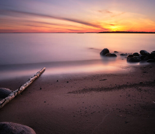 sunset at a lake with sandy beach in the foreground and stones in the water